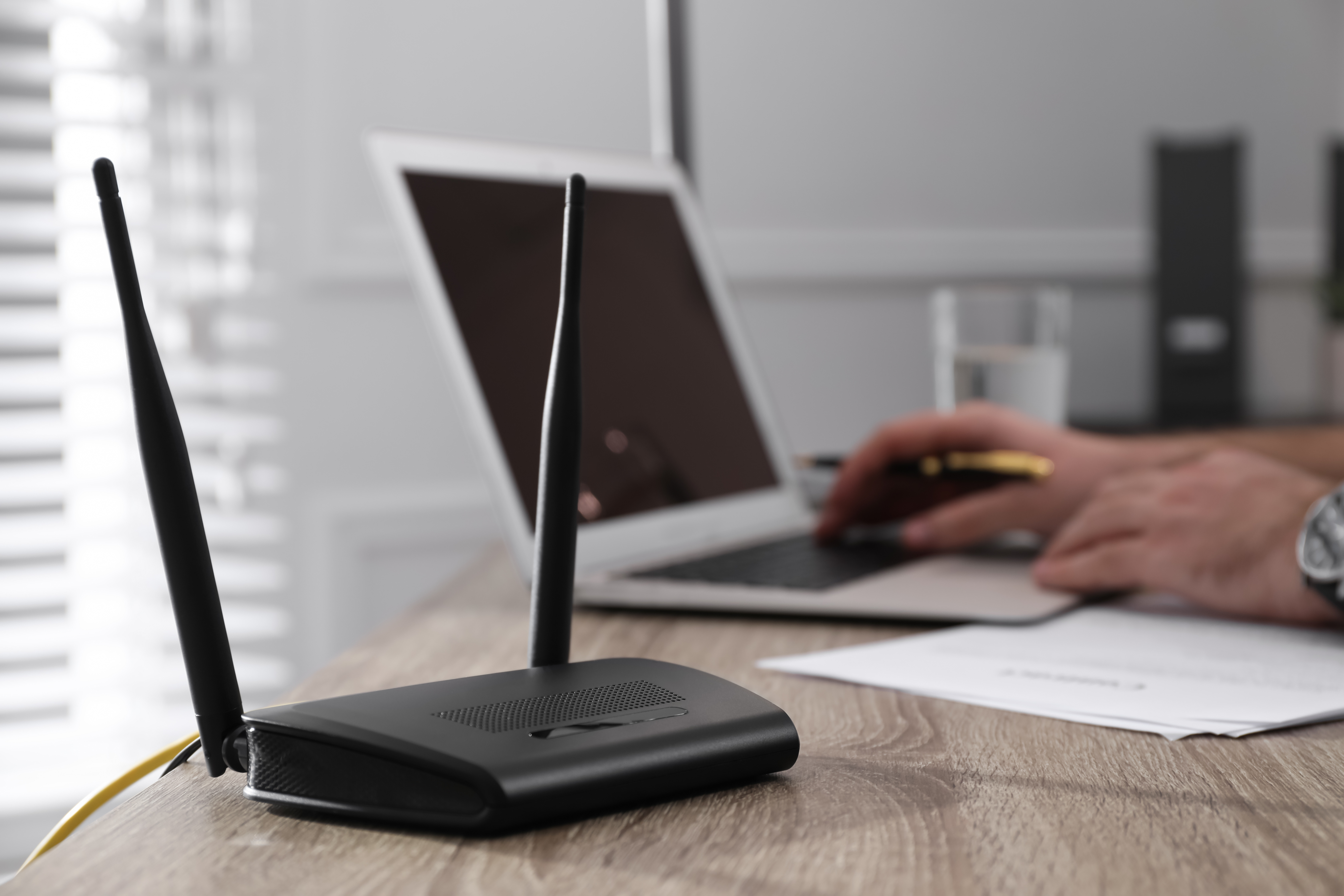 Man working with laptop in office, focus on connected router. Wireless internet communication gfast broadband